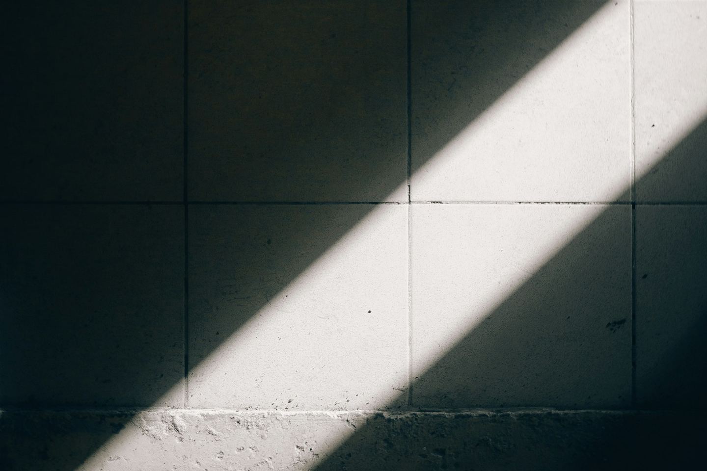 A diagonal beam of sunlight illuminates a tiled wall.
