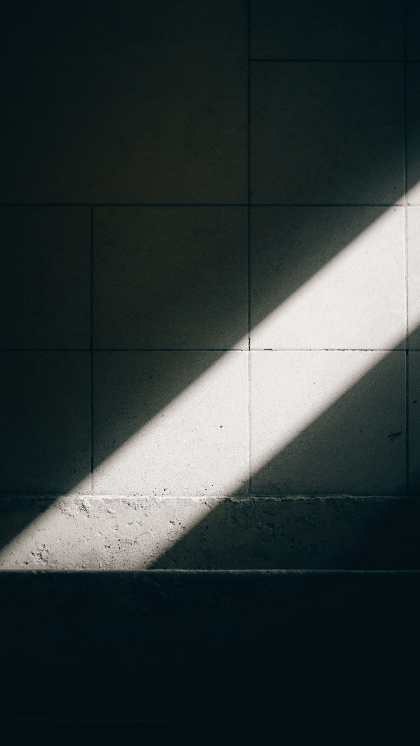 A diagonal beam of sunlight illuminates a tiled wall.