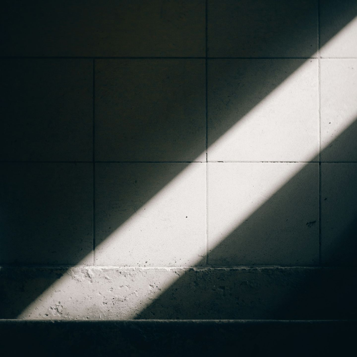 A diagonal beam of sunlight illuminates a tiled wall.