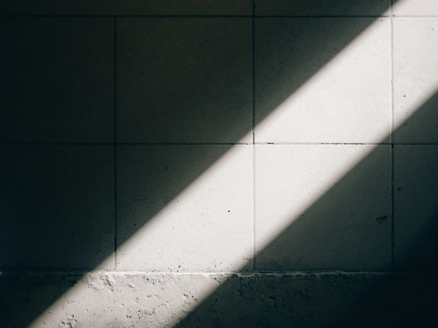 A diagonal beam of sunlight illuminates a tiled wall.