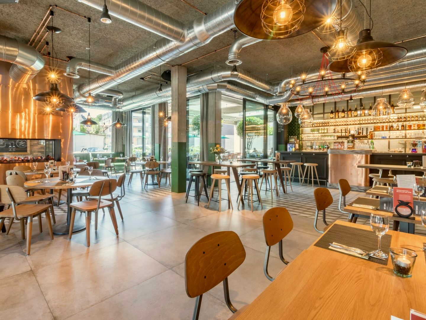Wooden tables and chairs along the wall of a bright café, the seats with their backs to the wall.