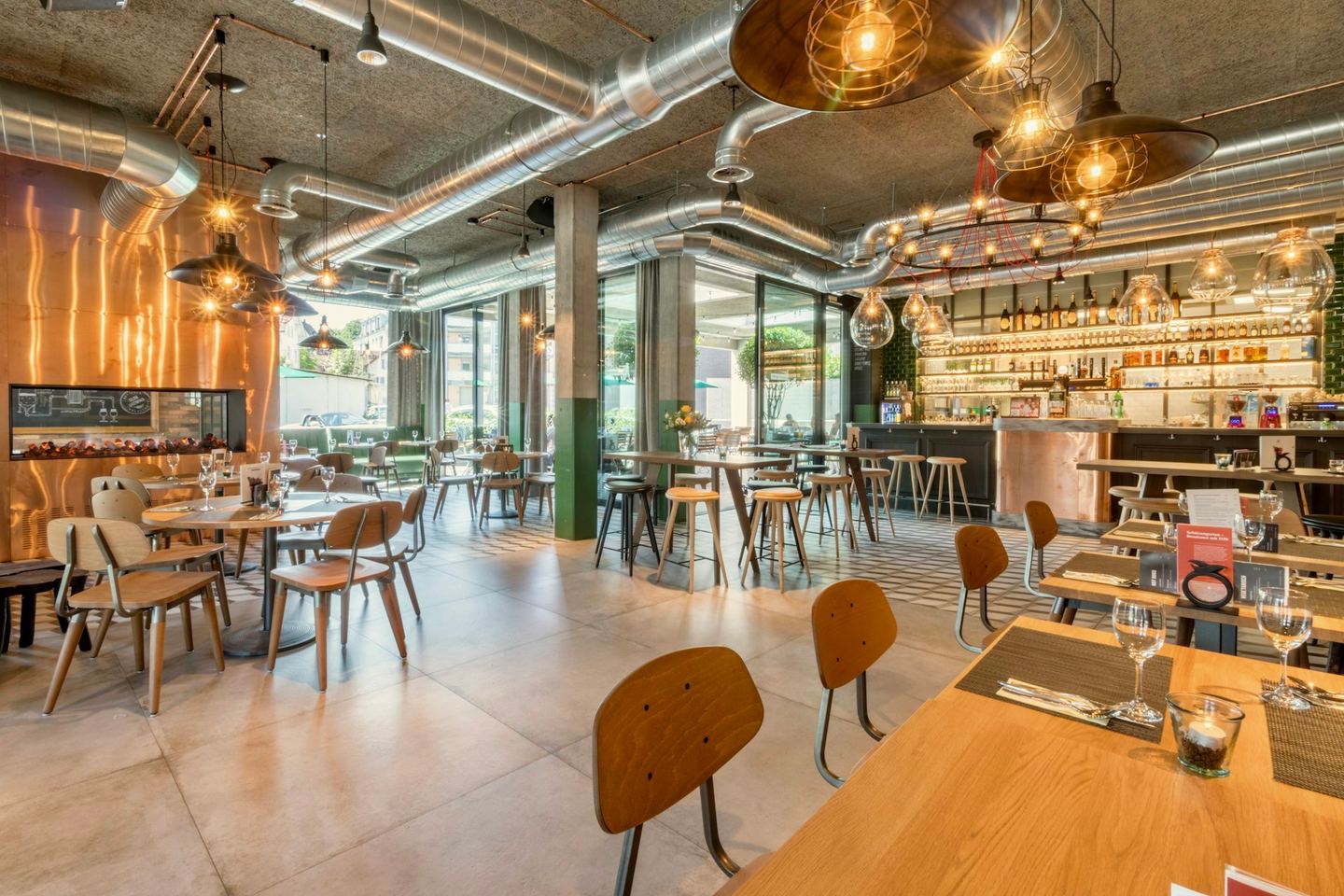Wooden tables and chairs along the wall of a bright café, the seats with their backs to the wall.