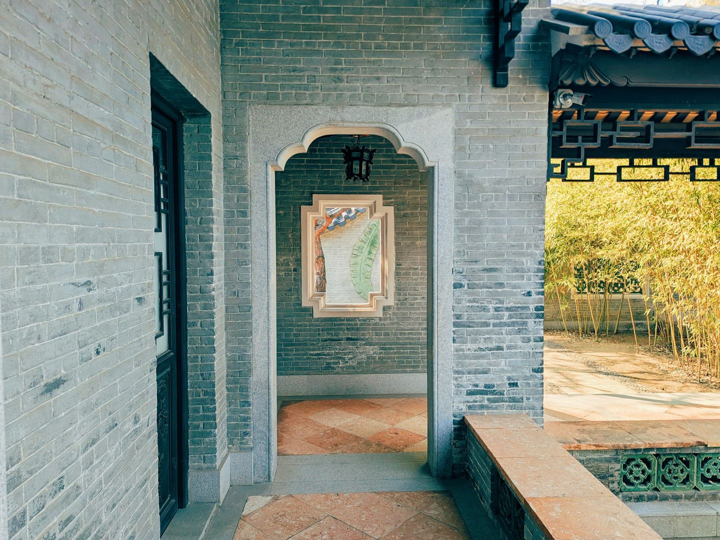 A brick courtyard of a Lingnan garden, its doorway opening onto bamboo in sunlight.