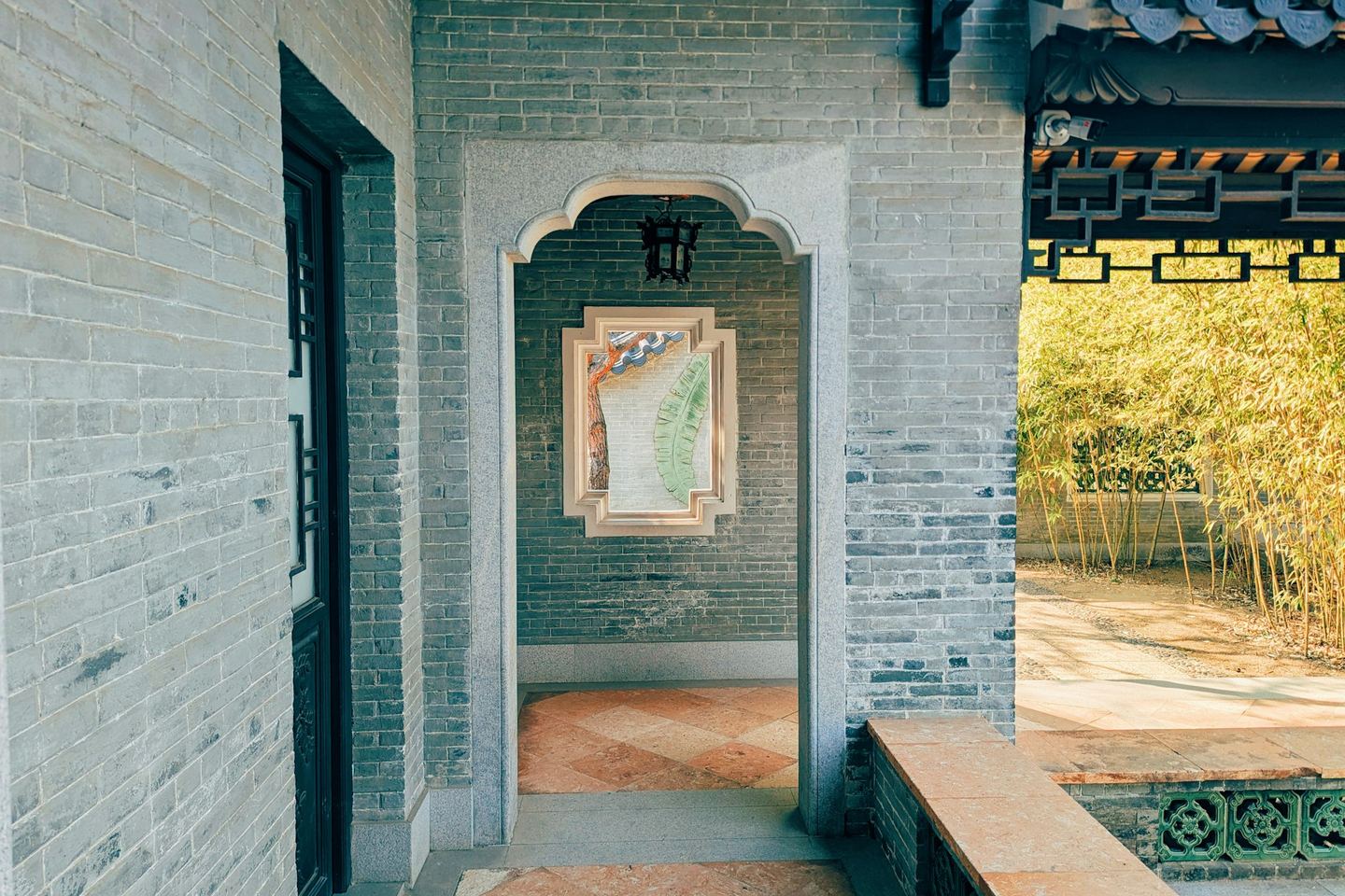 A brick courtyard of a Lingnan garden, its doorway opening onto bamboo in sunlight.