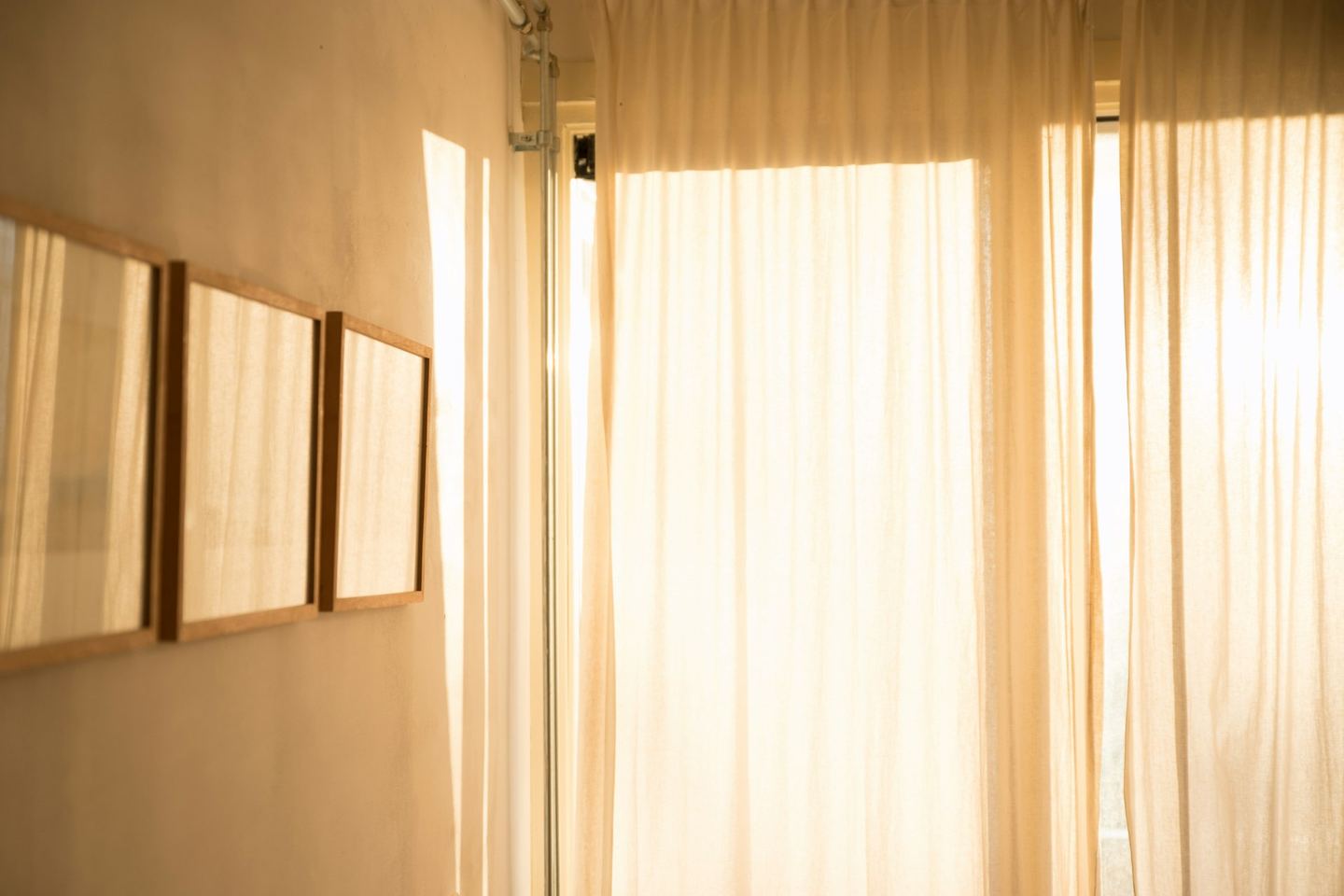 Morning light through white curtains in a pale room with framed pictures.