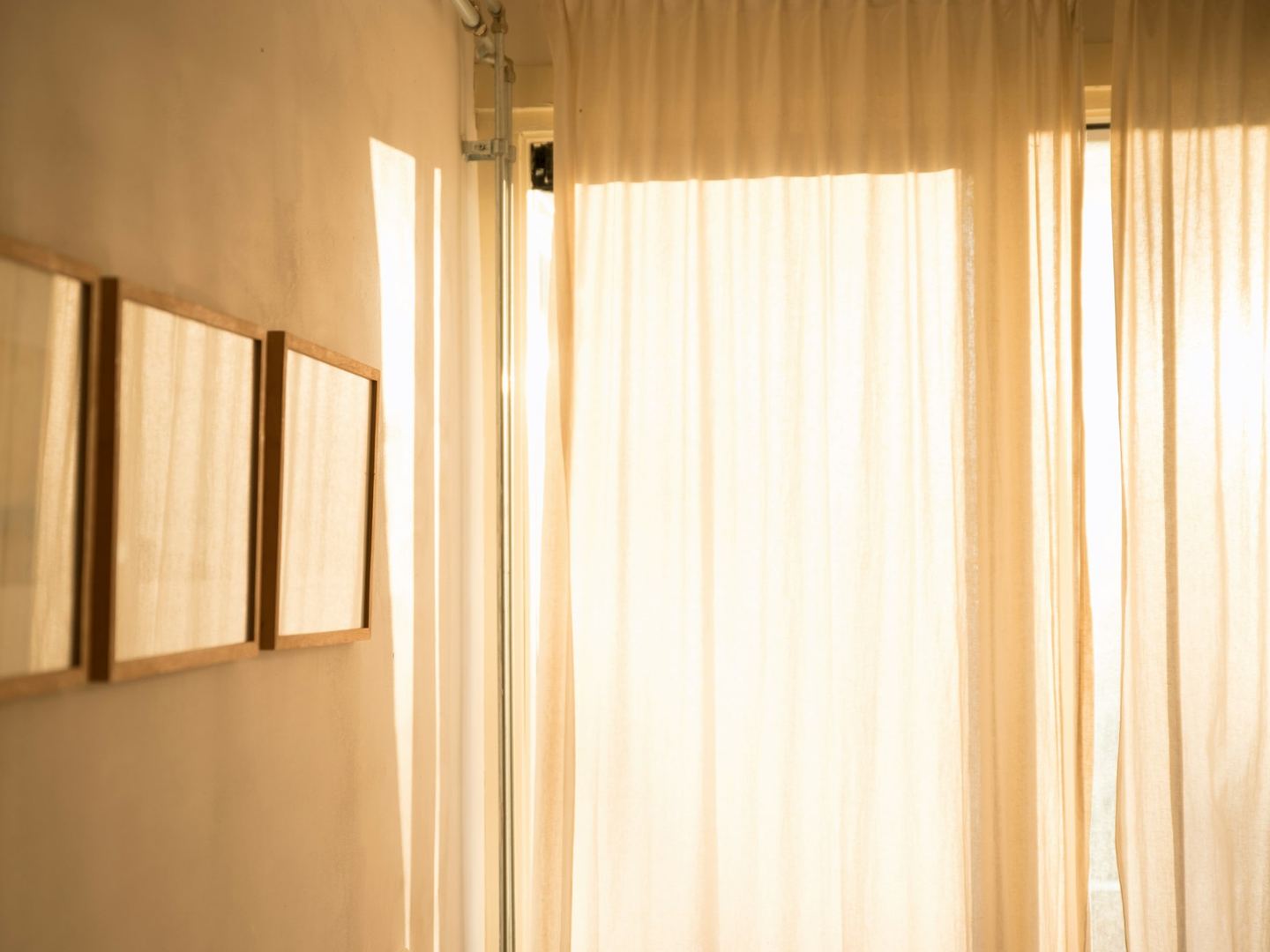 Morning light through white curtains in a pale room with framed pictures.