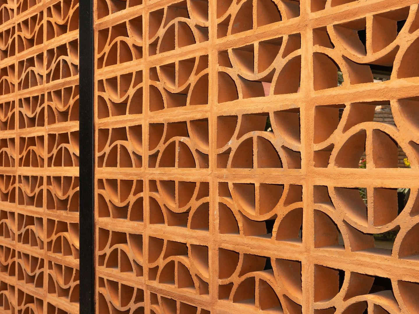 A terracotta screen of repeated geometric openings.