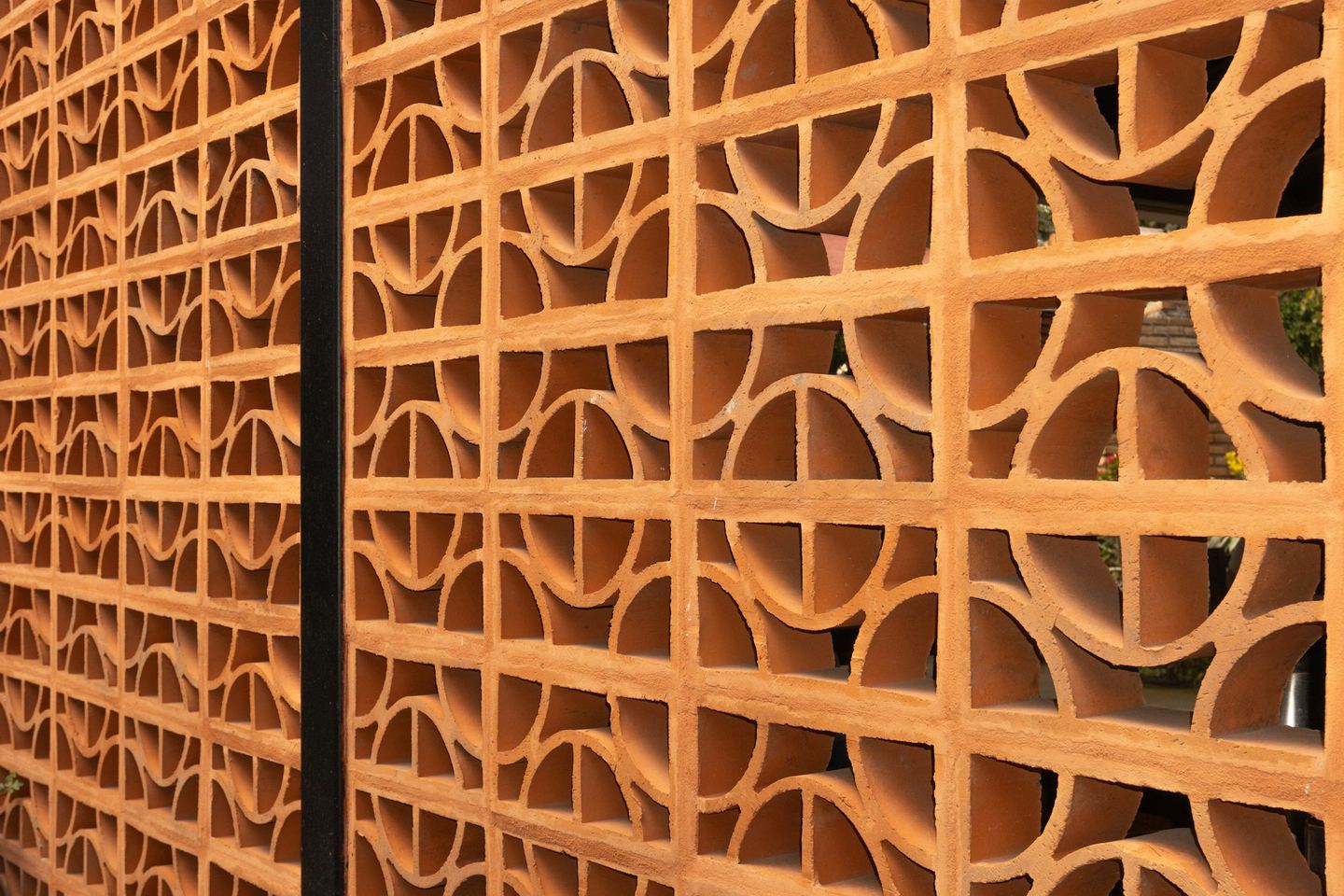 A terracotta screen of repeated geometric openings.