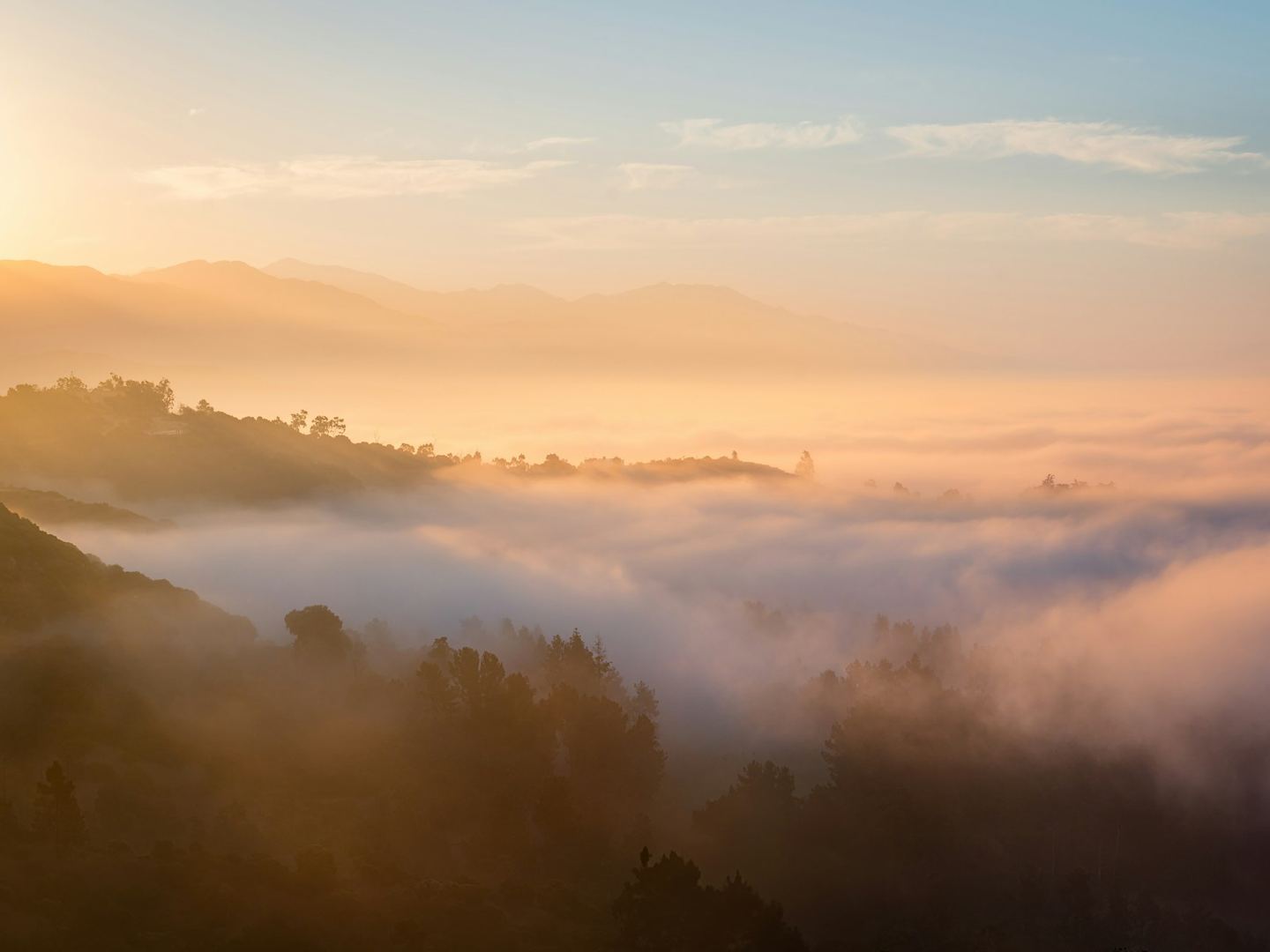 Golden dawn light over ranges of misty mountains, one behind another.