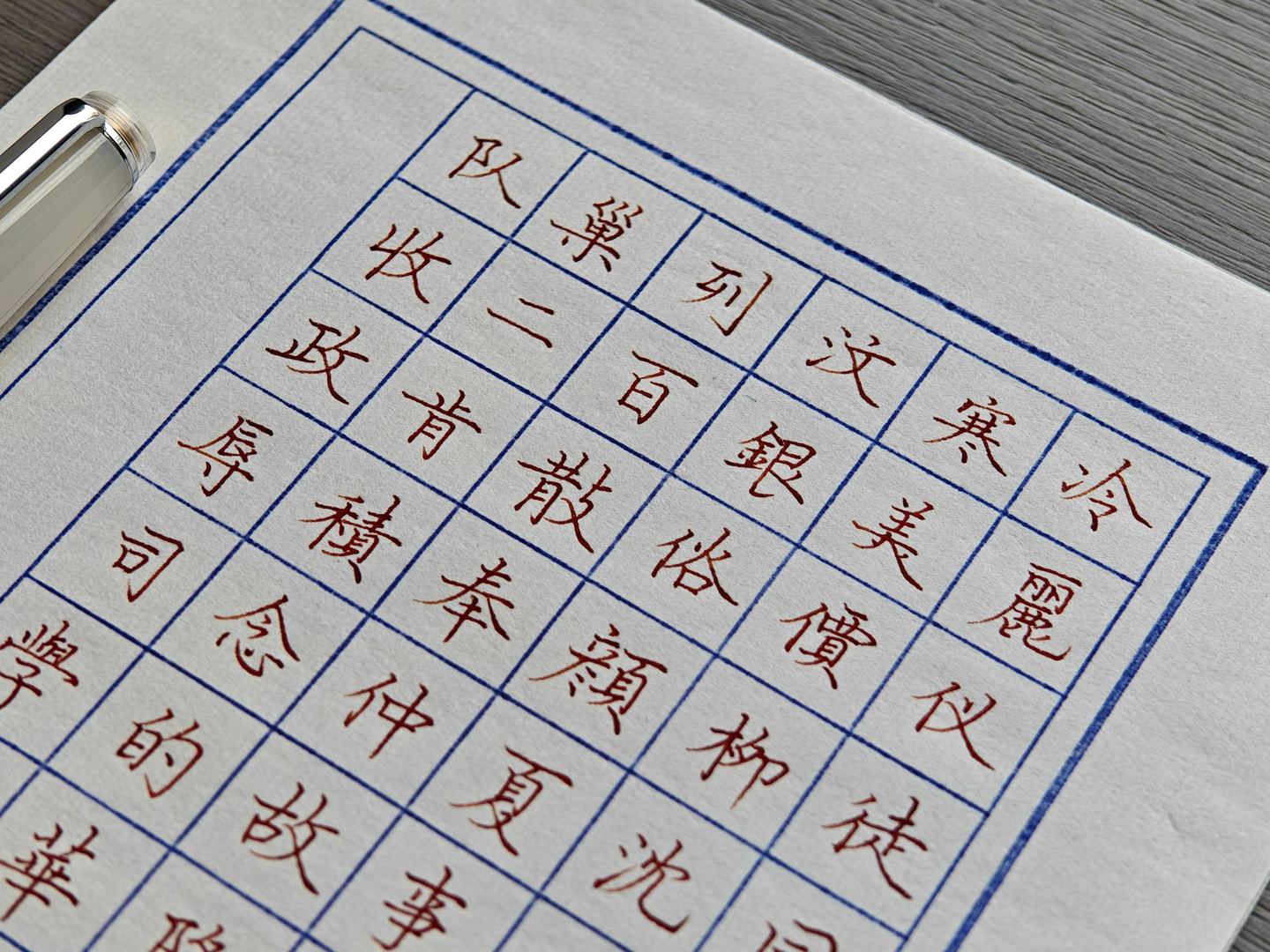 Handwritten Chinese characters in a grid on ruled paper, a pen beside them.
