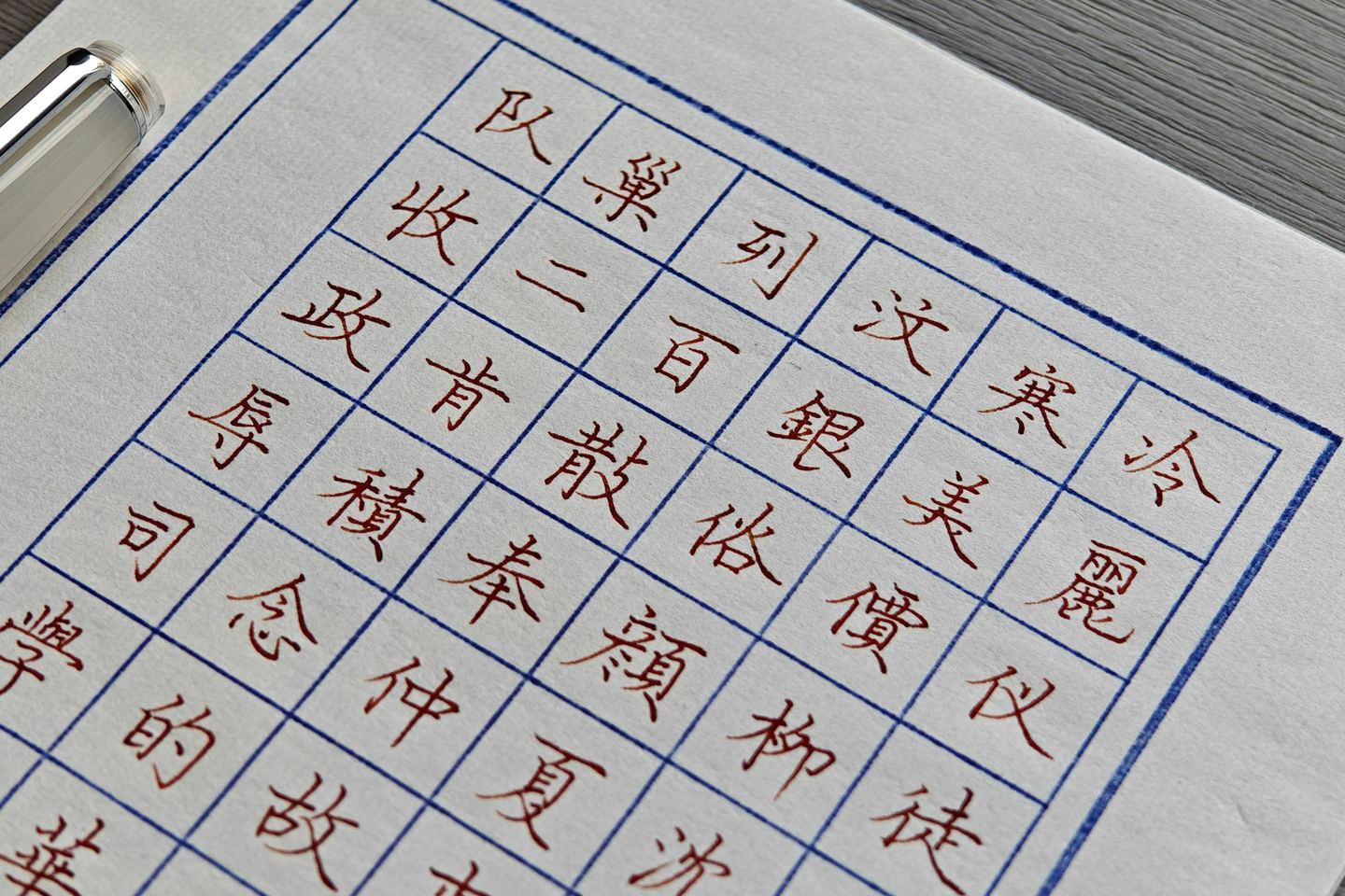 Handwritten Chinese characters in a grid on ruled paper, a pen beside them.