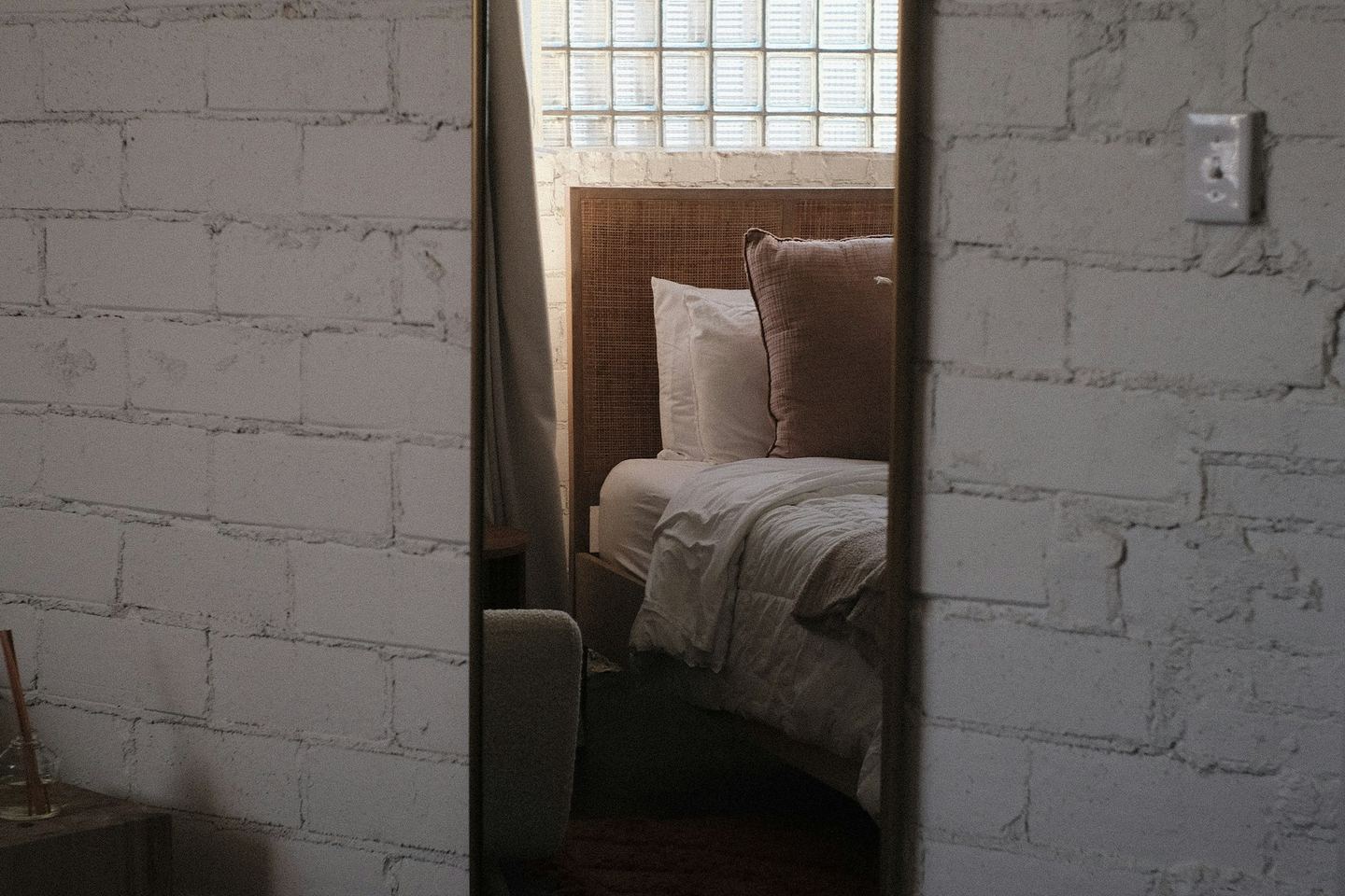 A mirror on a white brick wall reflecting a bed.