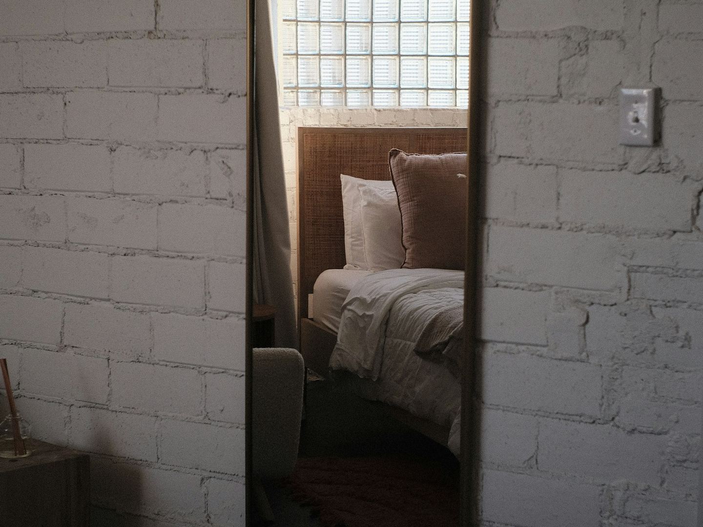 A mirror on a white brick wall reflecting a bed.