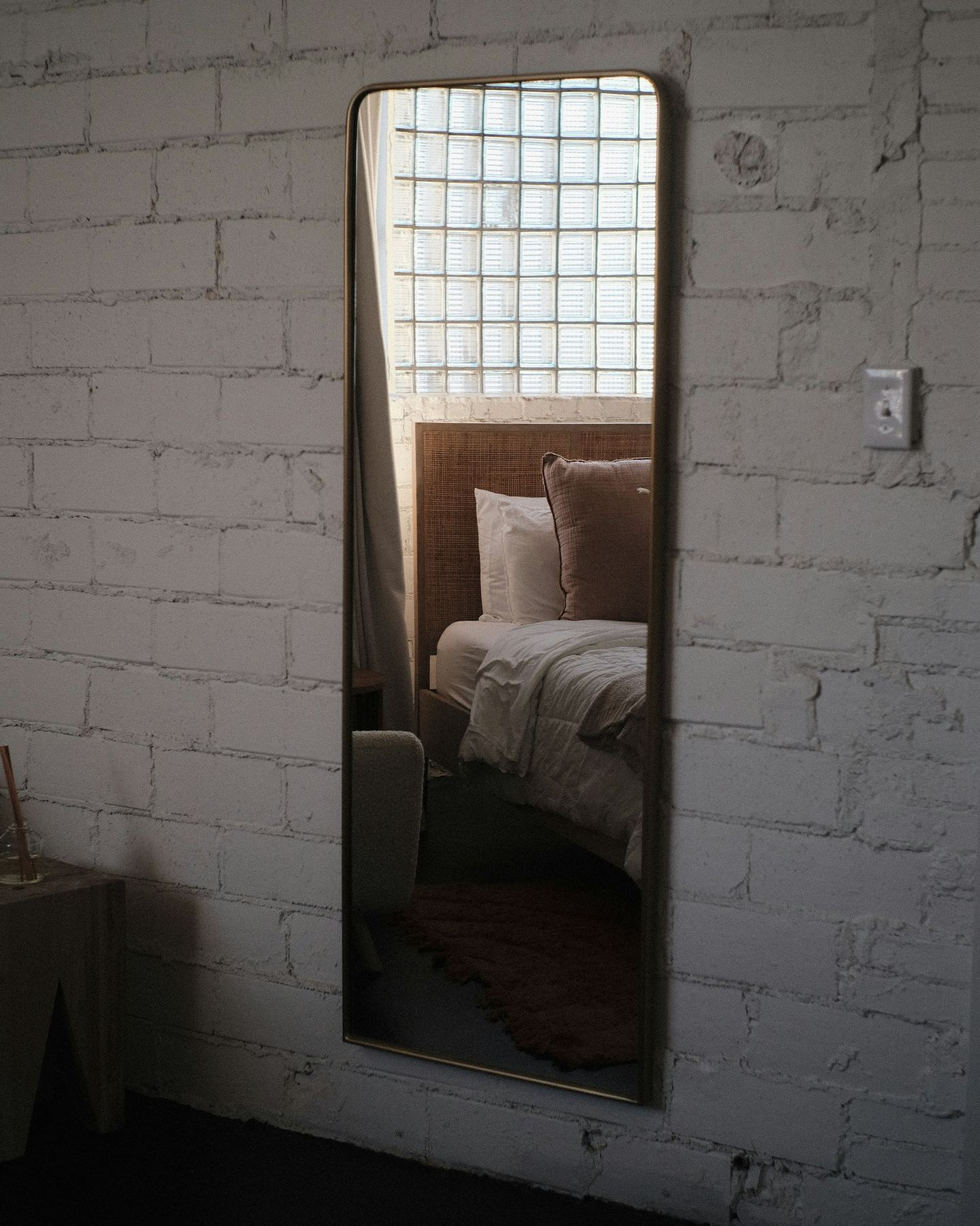 A mirror on a white brick wall reflecting a bed.