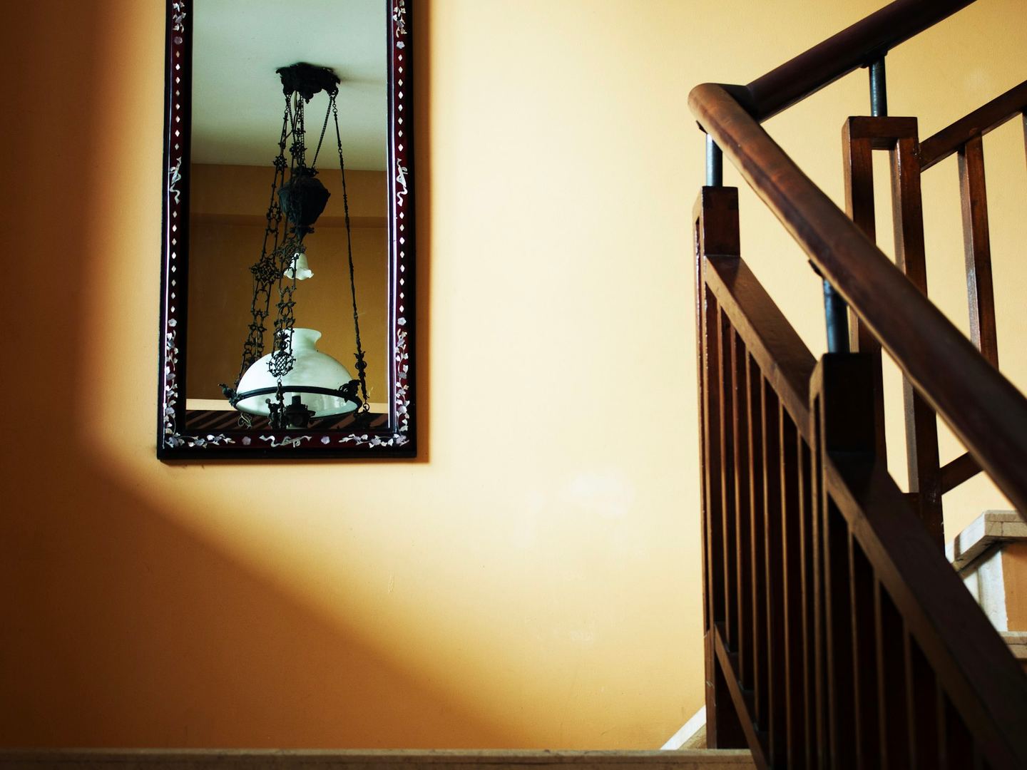 A framed mirror on a sunlit wall beside a wooden staircase.