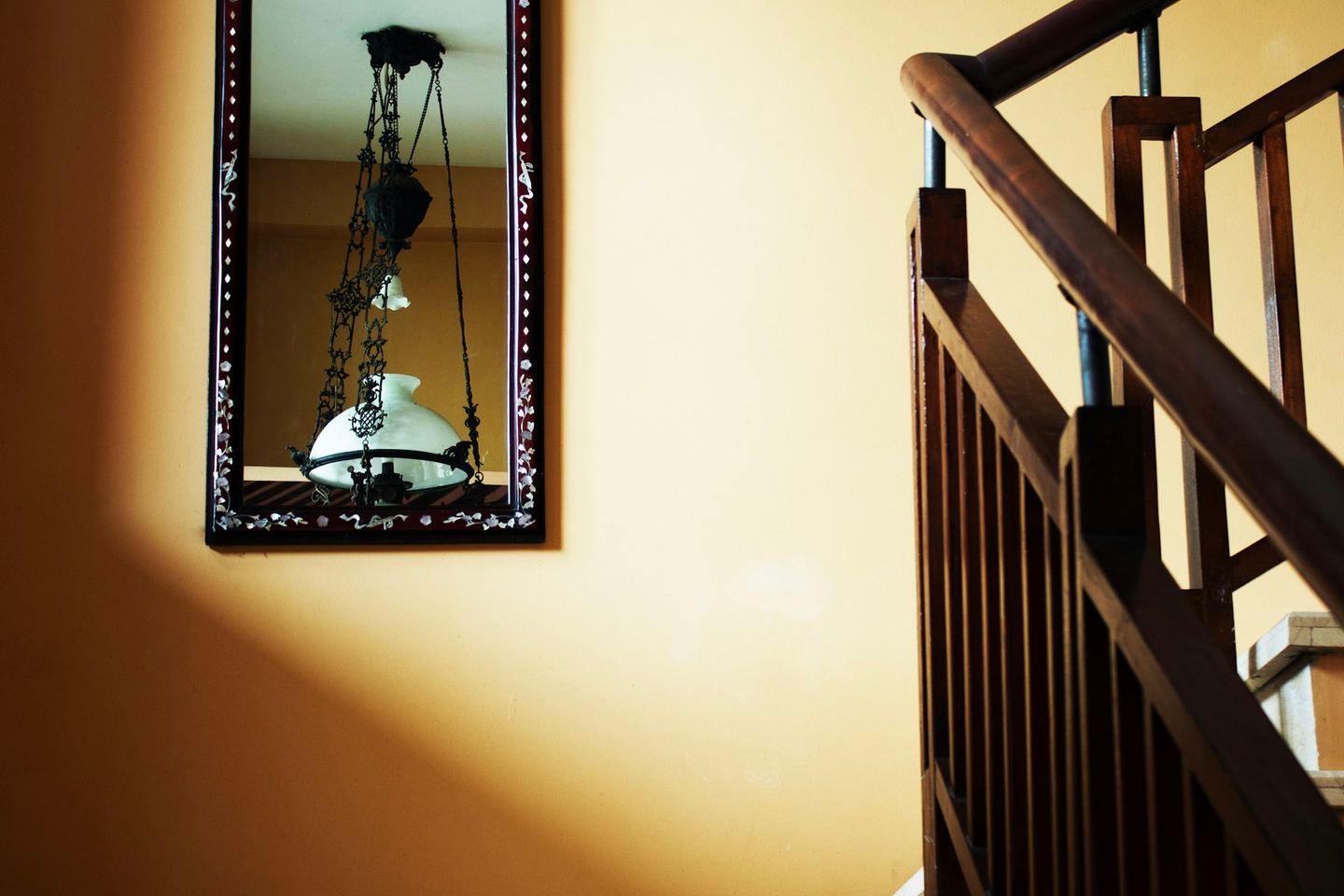 A framed mirror on a sunlit wall beside a wooden staircase.