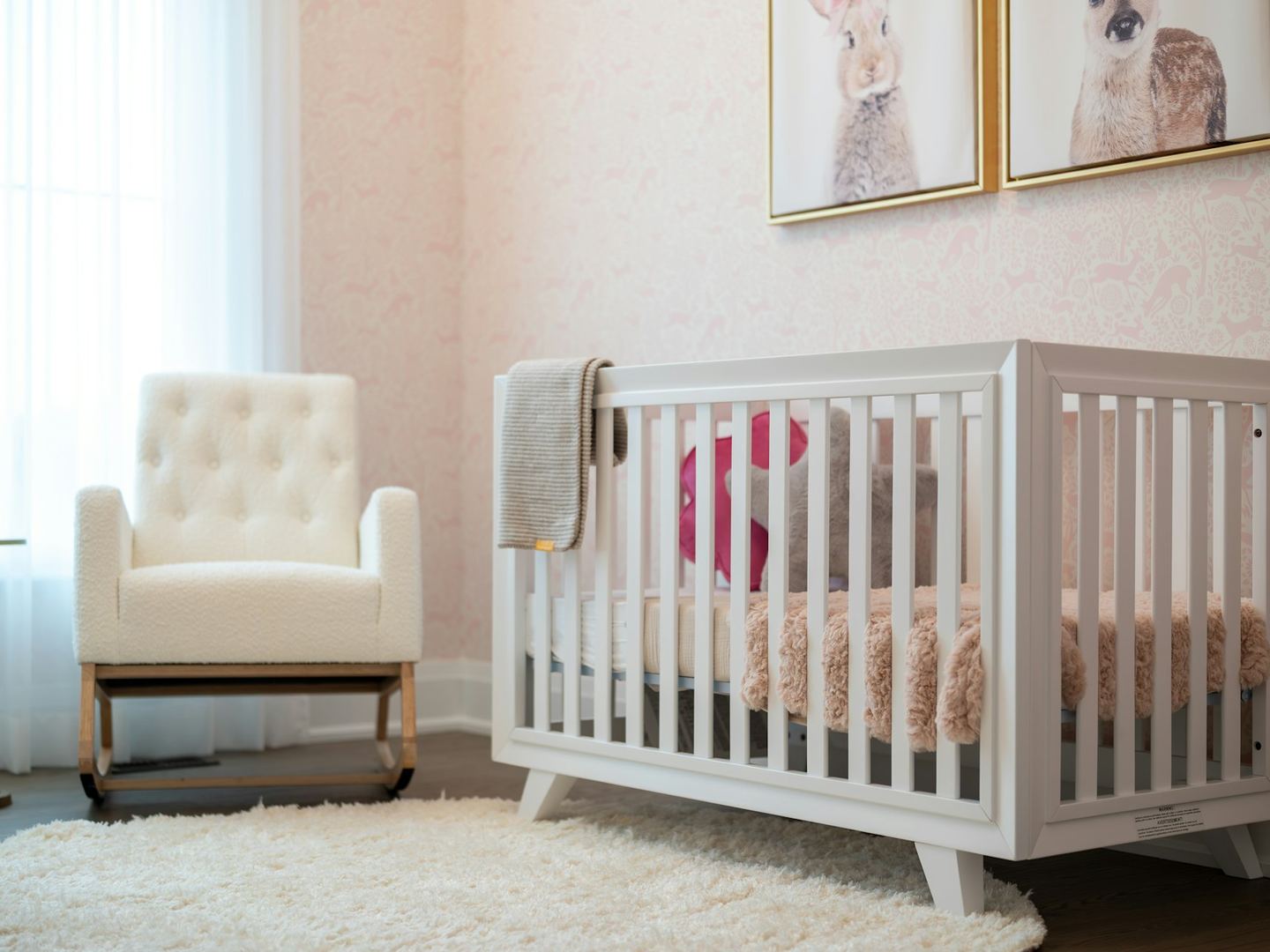 A white cot and a nursing chair in a pale nursery, light through the curtain.