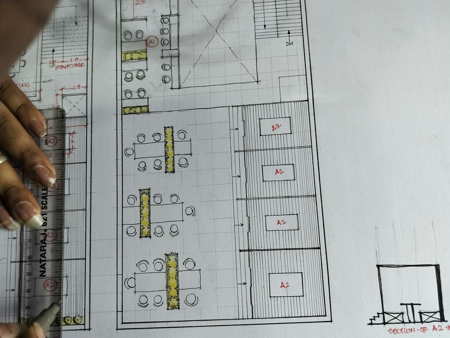 A hand with a ruler drawing a floor plan in ink on white paper.