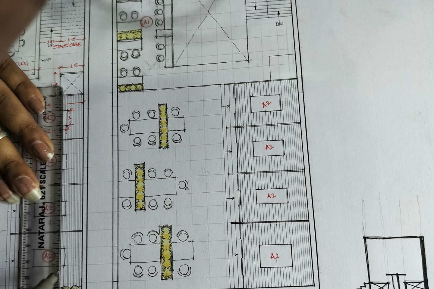 A hand on a drawn floor plan with red marks and a scale rule.