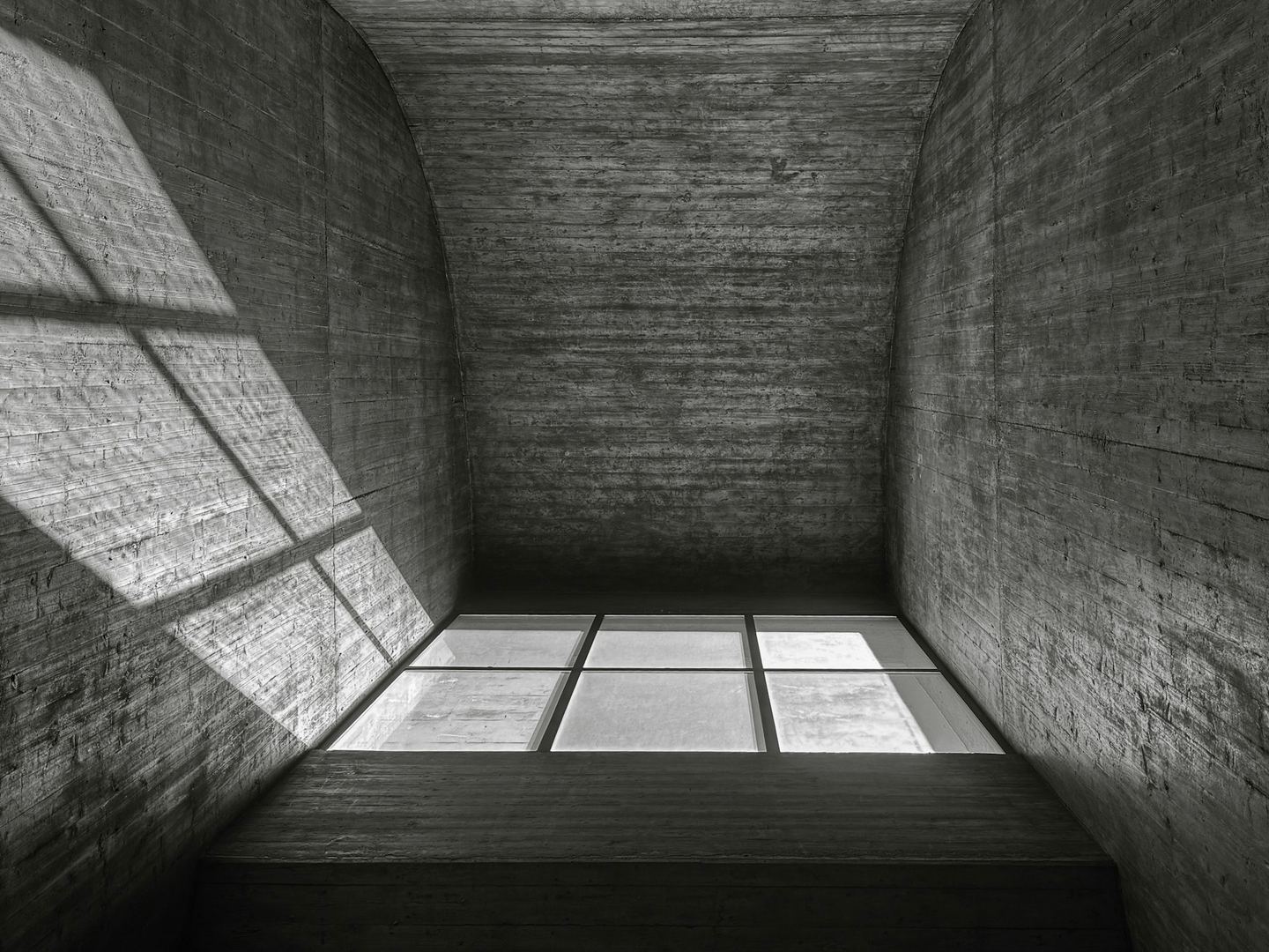 Sunlight enters a bare concrete room through a single window, drawing a bright rectangle on the floor.
