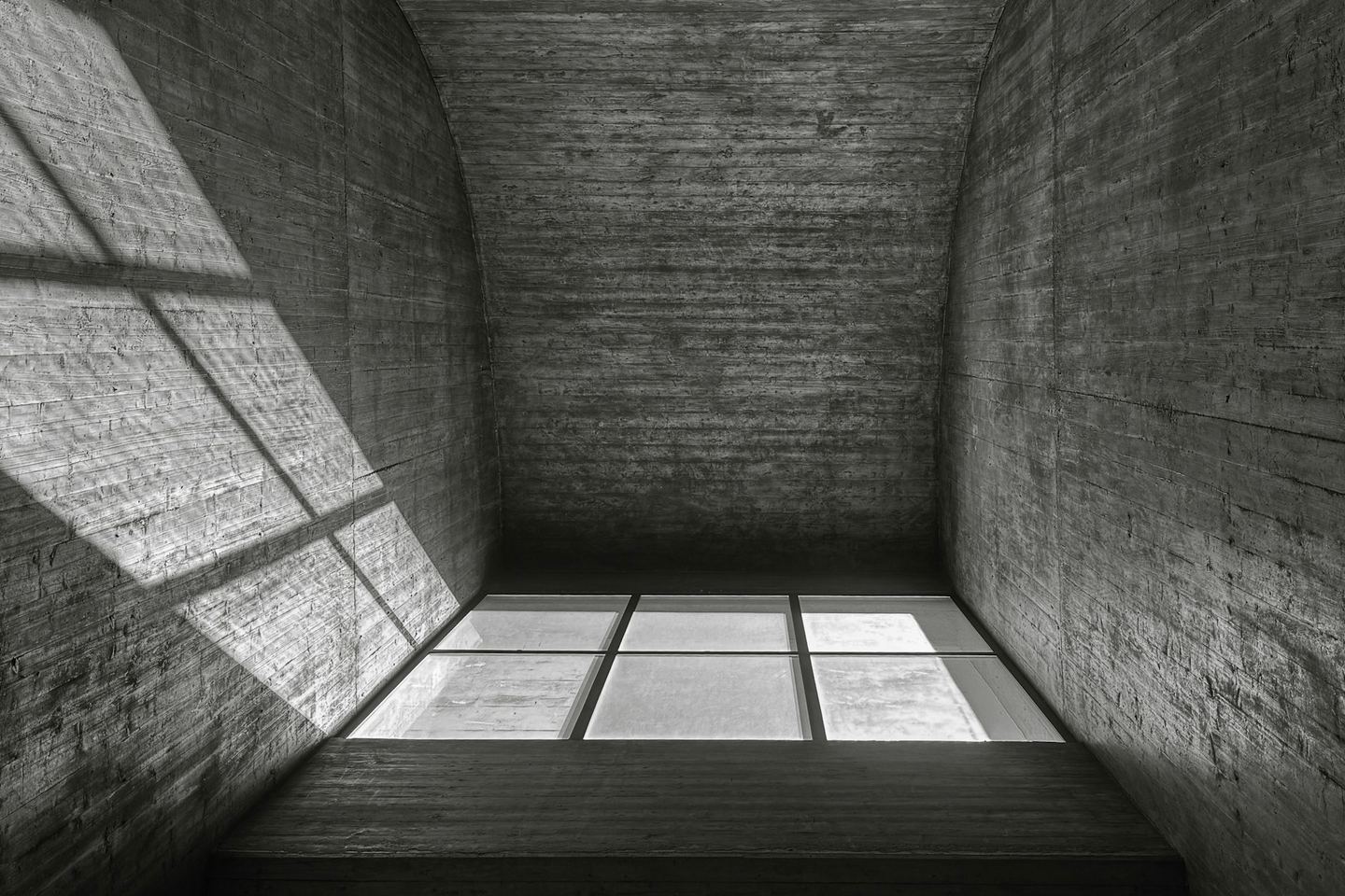 Sunlight enters a bare concrete room through a single window, drawing a bright rectangle on the floor.