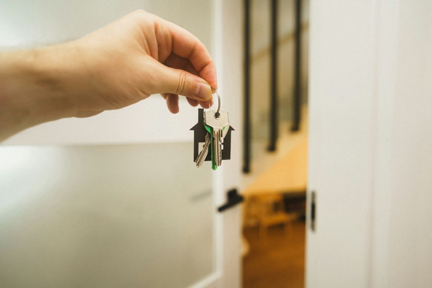 A hand holding out a bunch of house keys at an open white door, a lit room beyond.