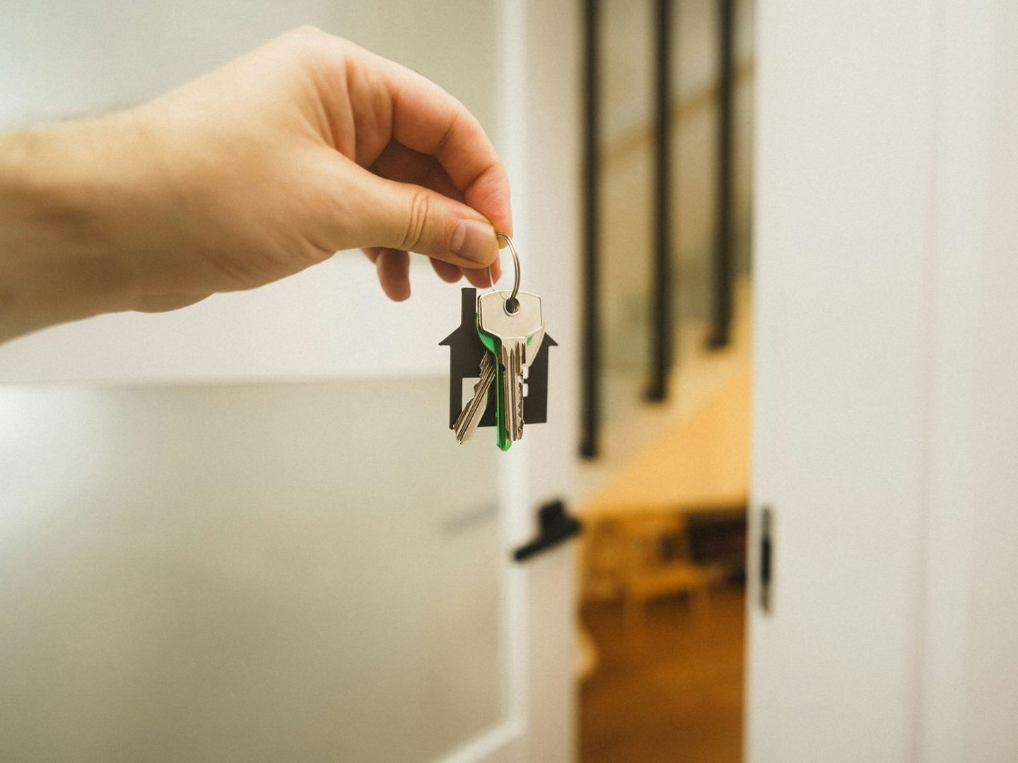 A hand holding out a bunch of house keys at an open white door, a lit room beyond.
