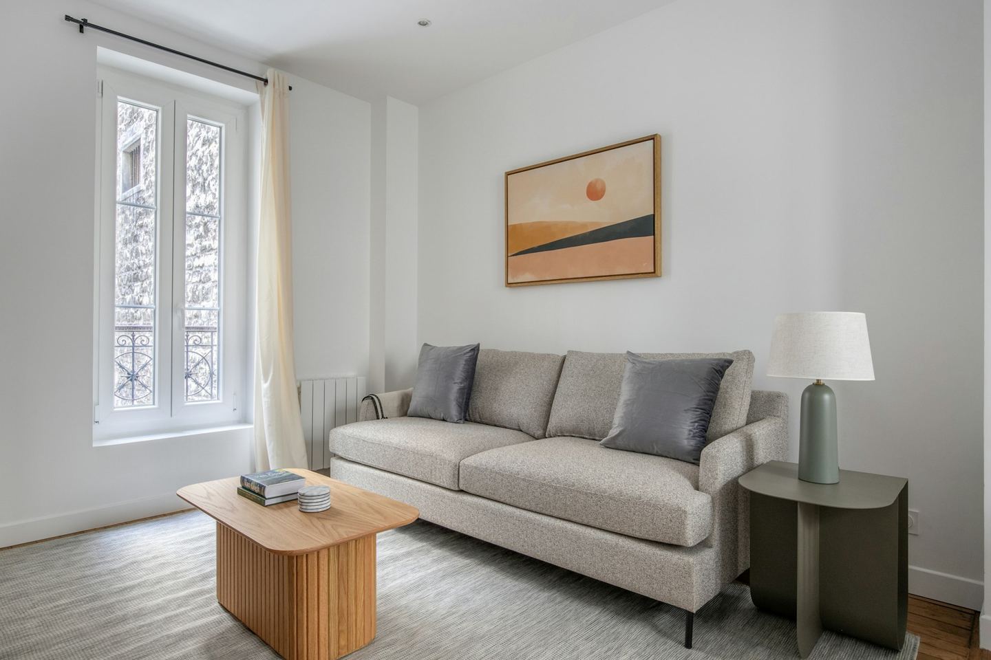 A bright living room with two sofas facing each other across a low table, a tall window at the side and a wall of framed pictures behind.