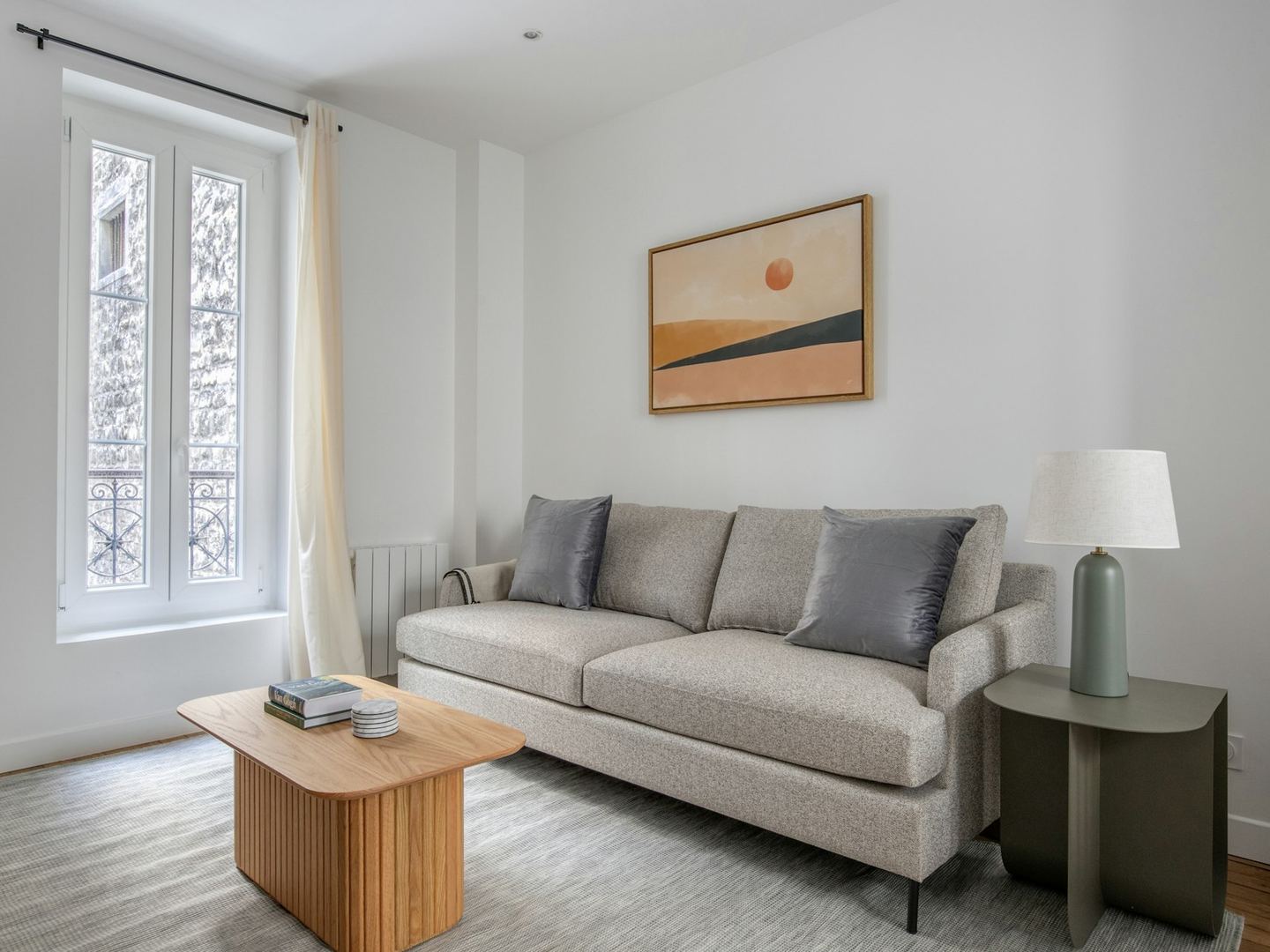A bright living room with two sofas facing each other across a low table, a tall window at the side and a wall of framed pictures behind.