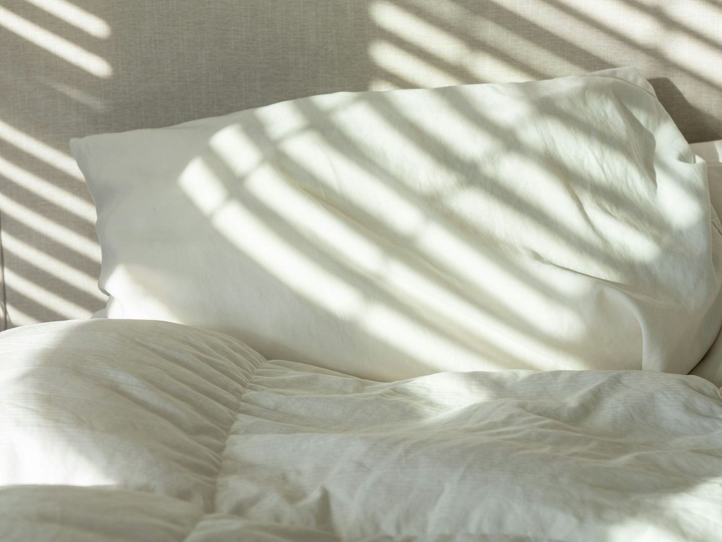 Morning light in stripes across a white pillow and duvet.