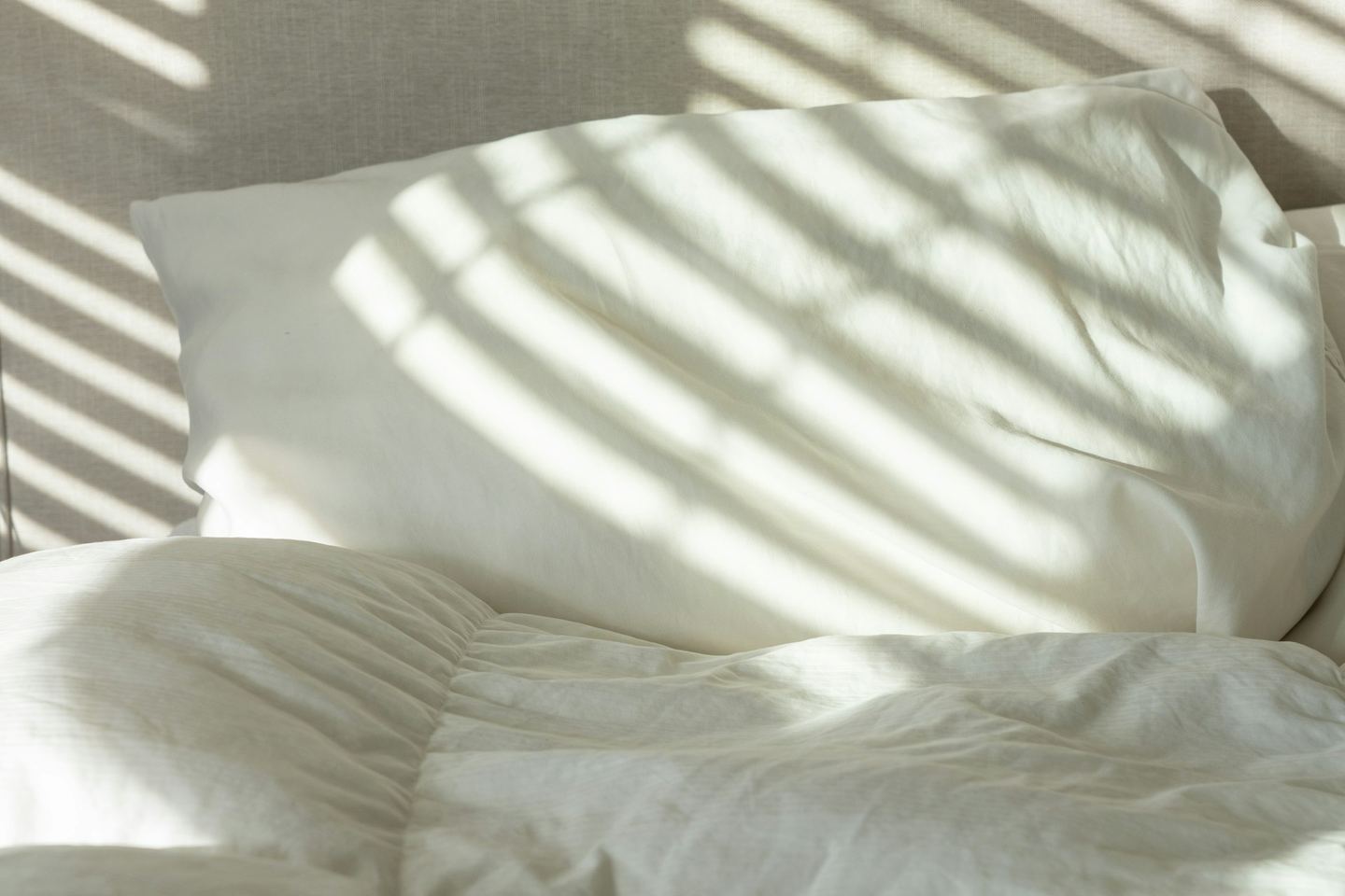 Morning light in stripes across a white pillow and duvet.