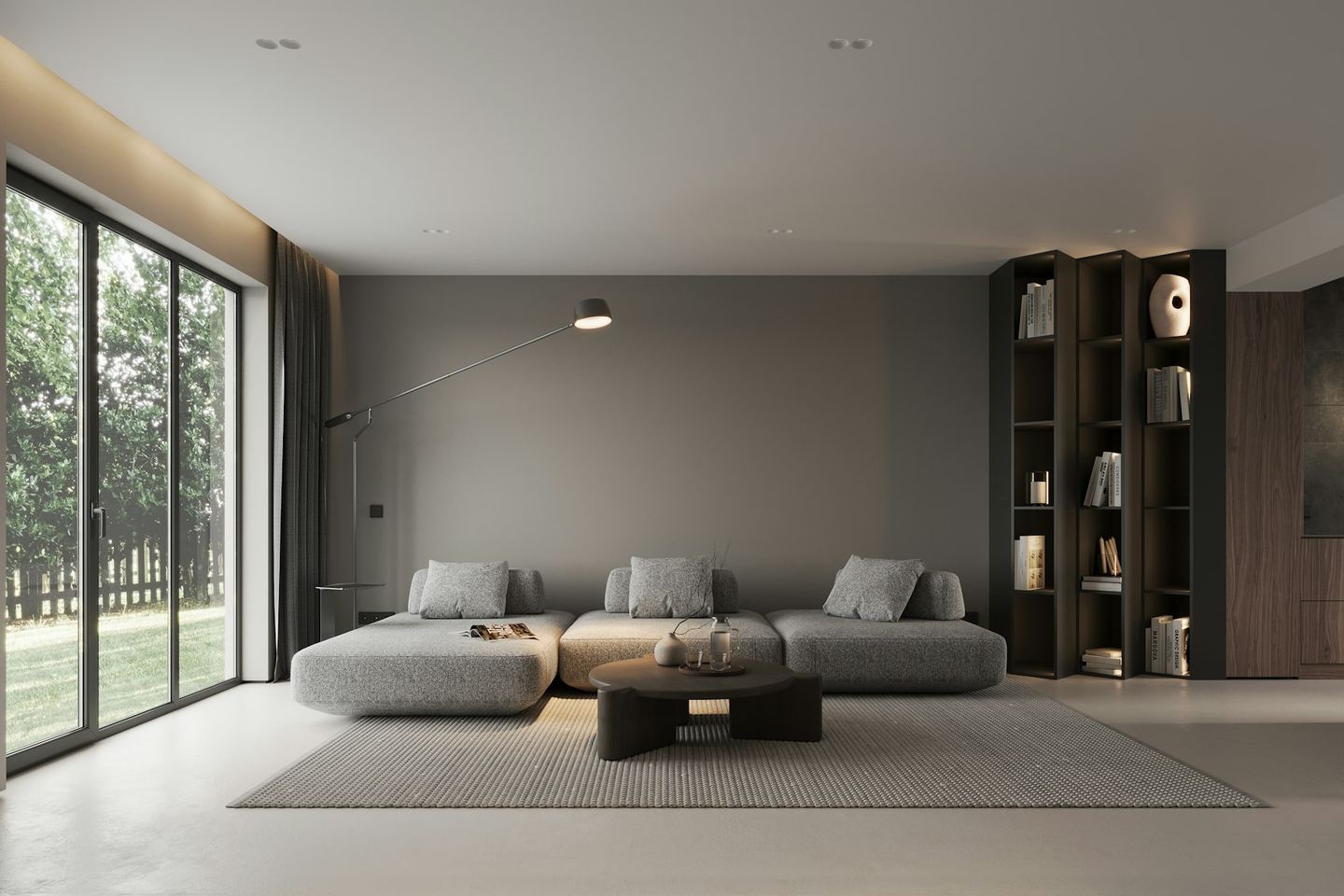 A low grey sofa in the middle of a large living room with a glass wall on one side.