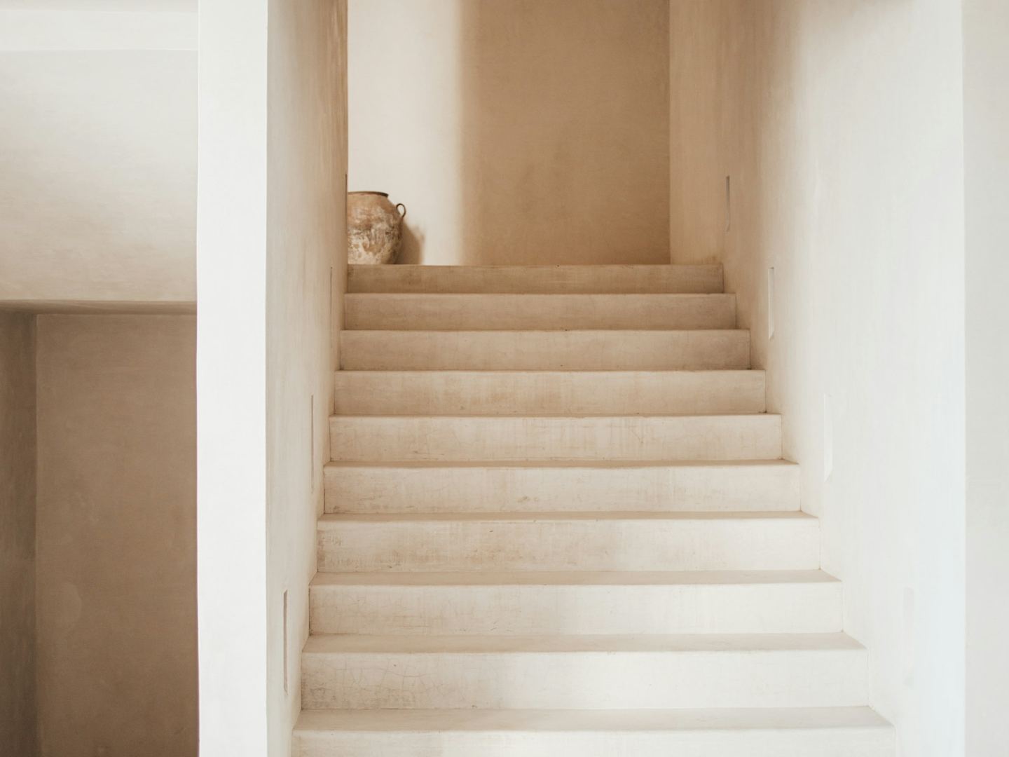 A minimalist staircase with white steps leading to a landing with a vase.