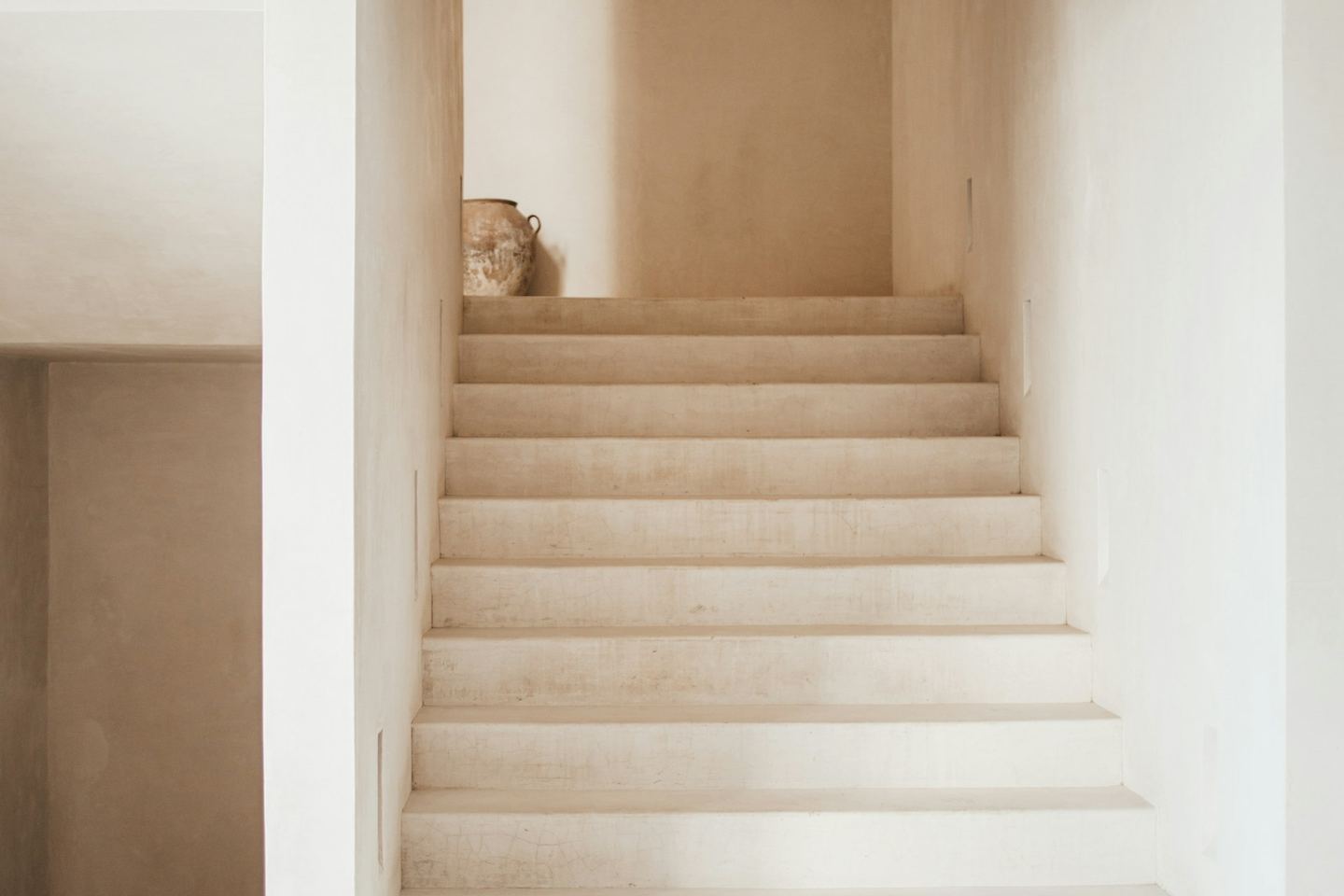 A minimalist staircase with white steps leading to a landing with a vase.