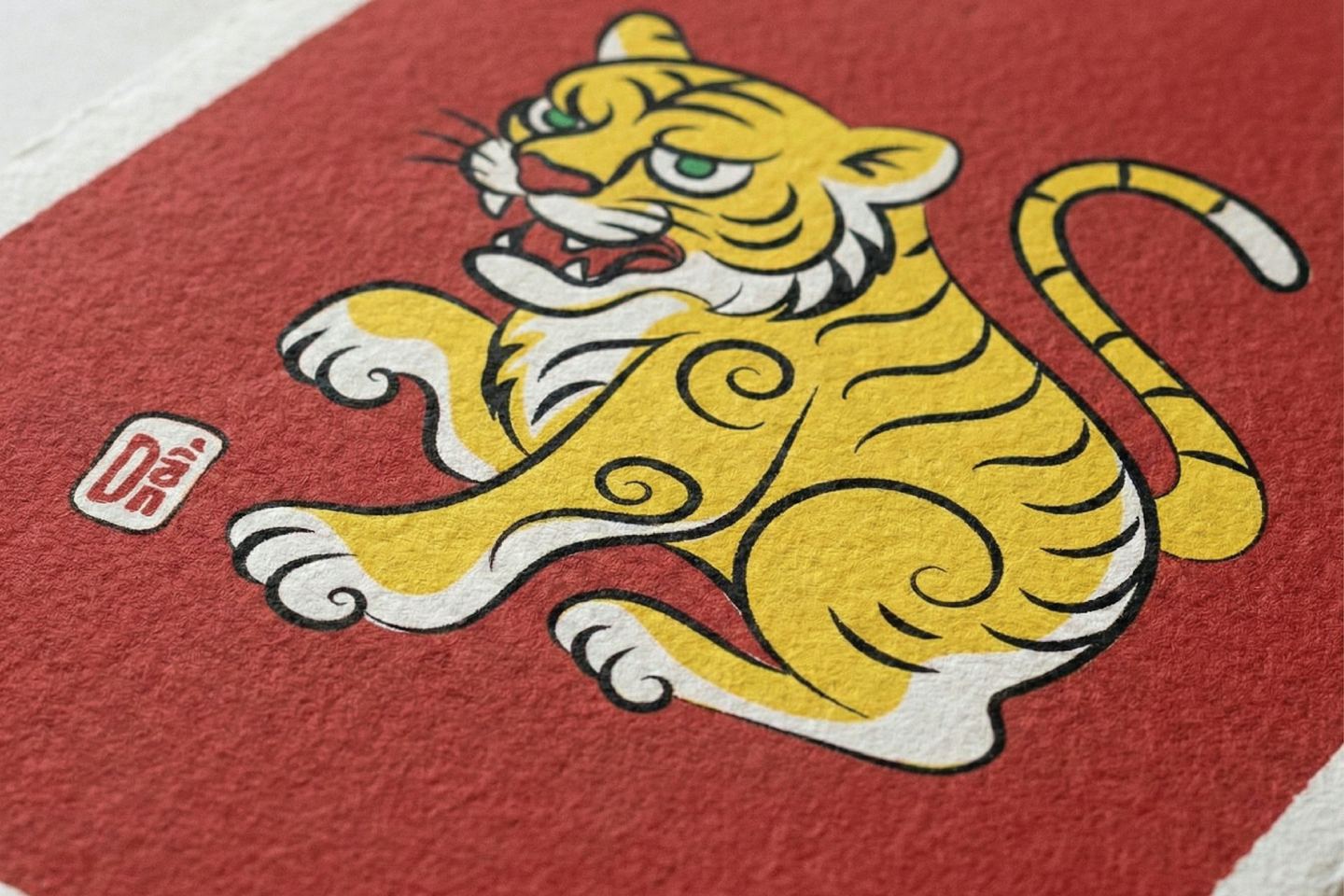A stylised yellow tiger printed on a red ground, with a small red seal beside it, on textured paper.