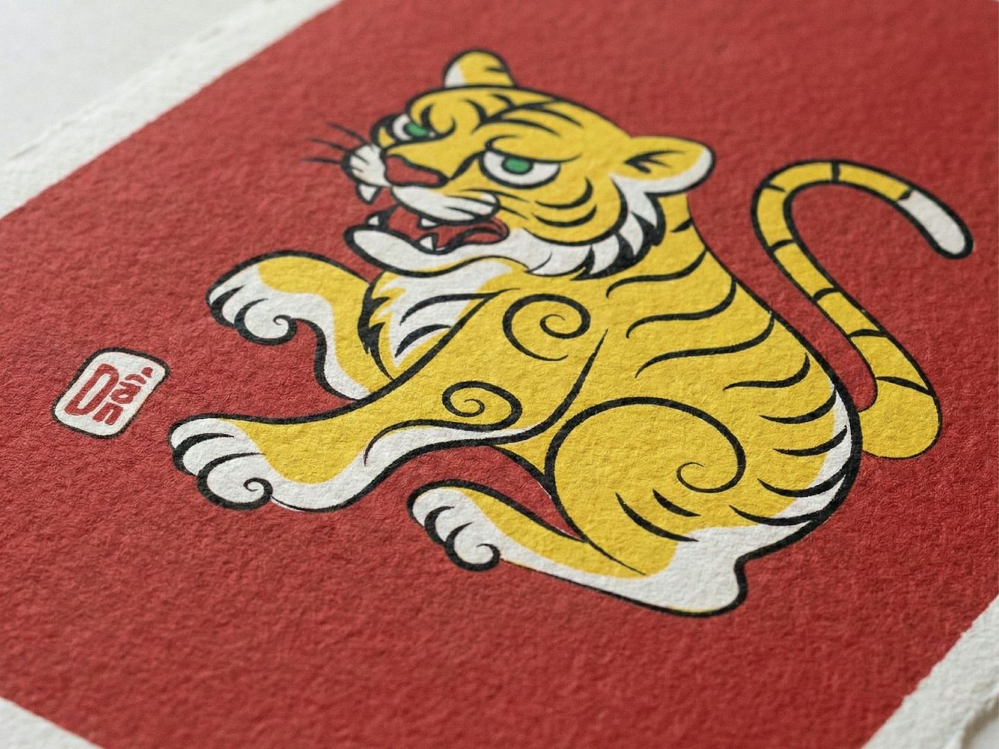 A stylised yellow tiger printed on a red ground, with a small red seal beside it, on textured paper.