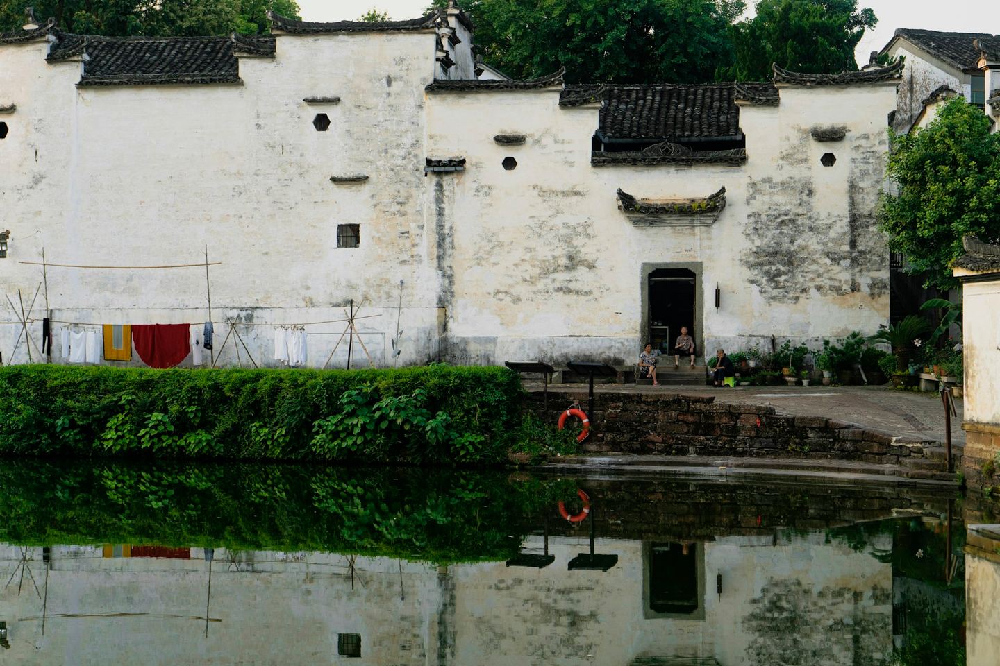 Tall whitewashed walls with stepped dark-tiled gables above a still pond, in a village of the lower Yangtze.