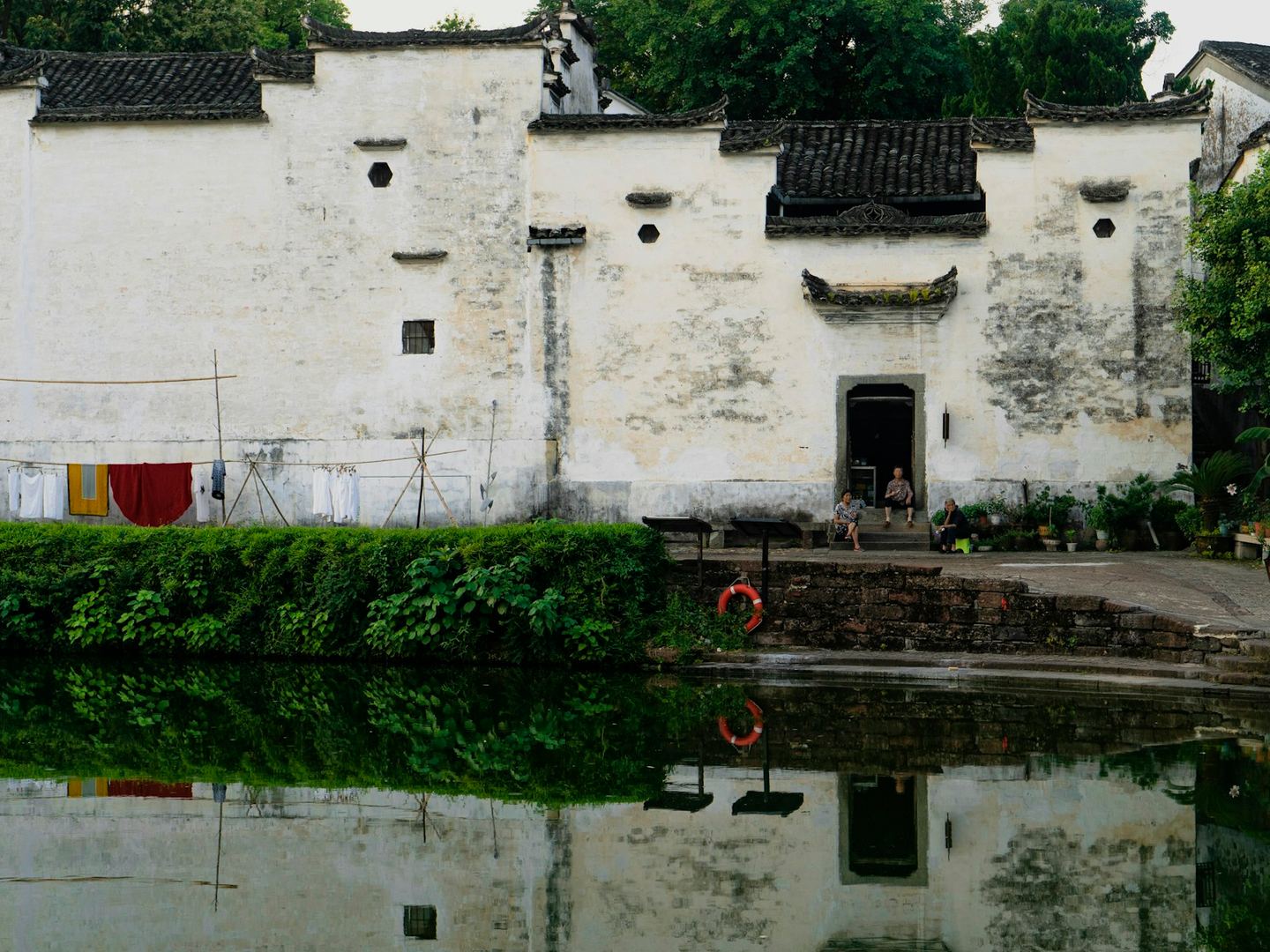 Tall whitewashed walls with stepped dark-tiled gables above a still pond, in a village of the lower Yangtze.