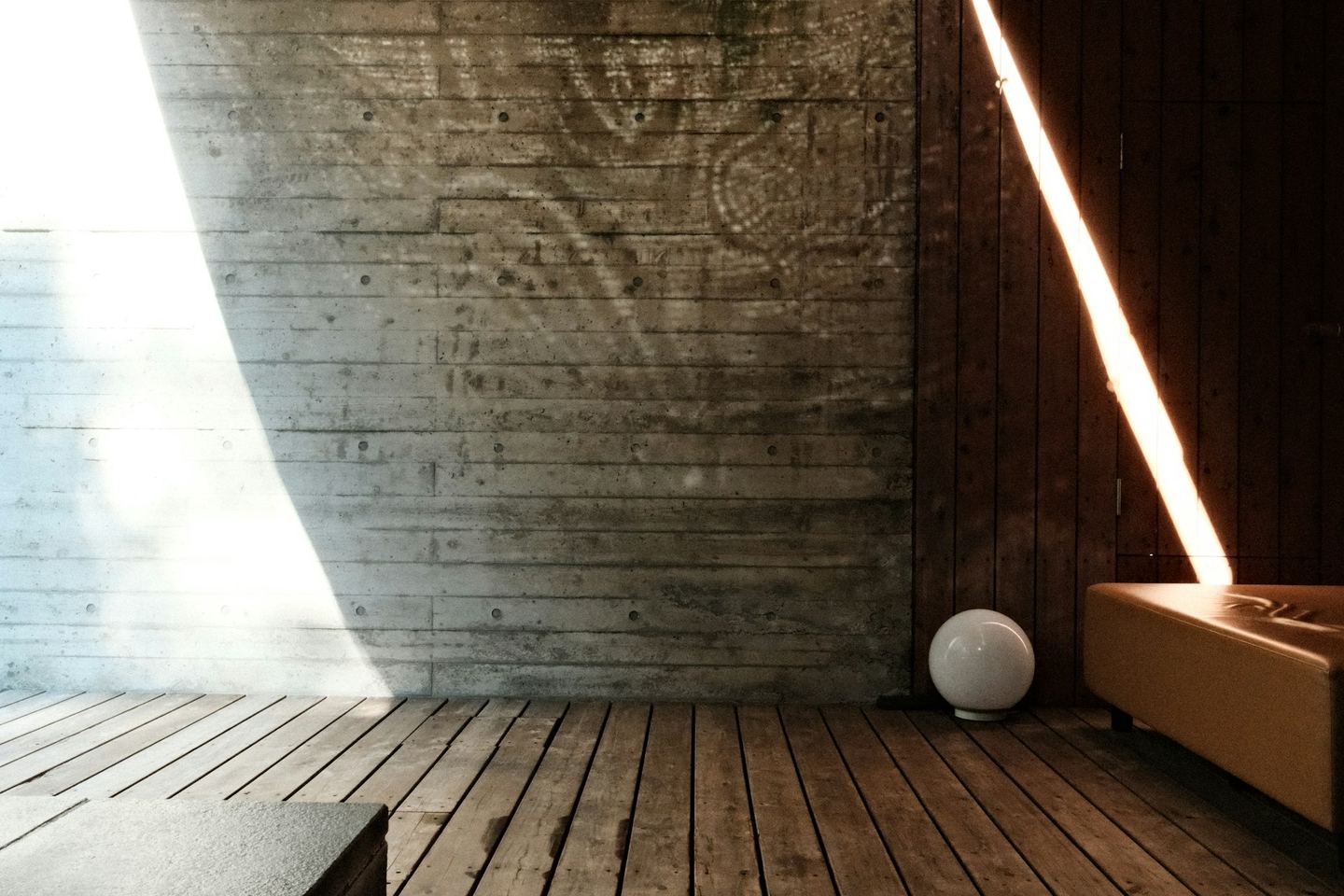 Sunlight across a concrete wall and a wooden floor, half the room lit and half in shade.