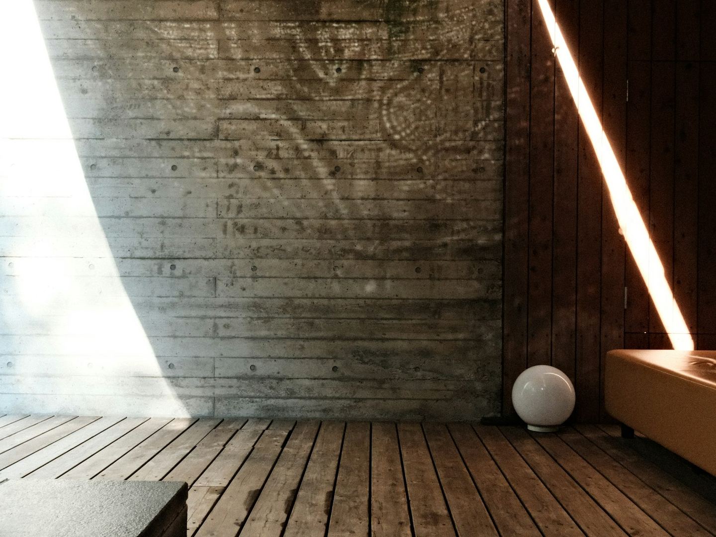 Sunlight across a concrete wall and a wooden floor, half the room lit and half in shade.