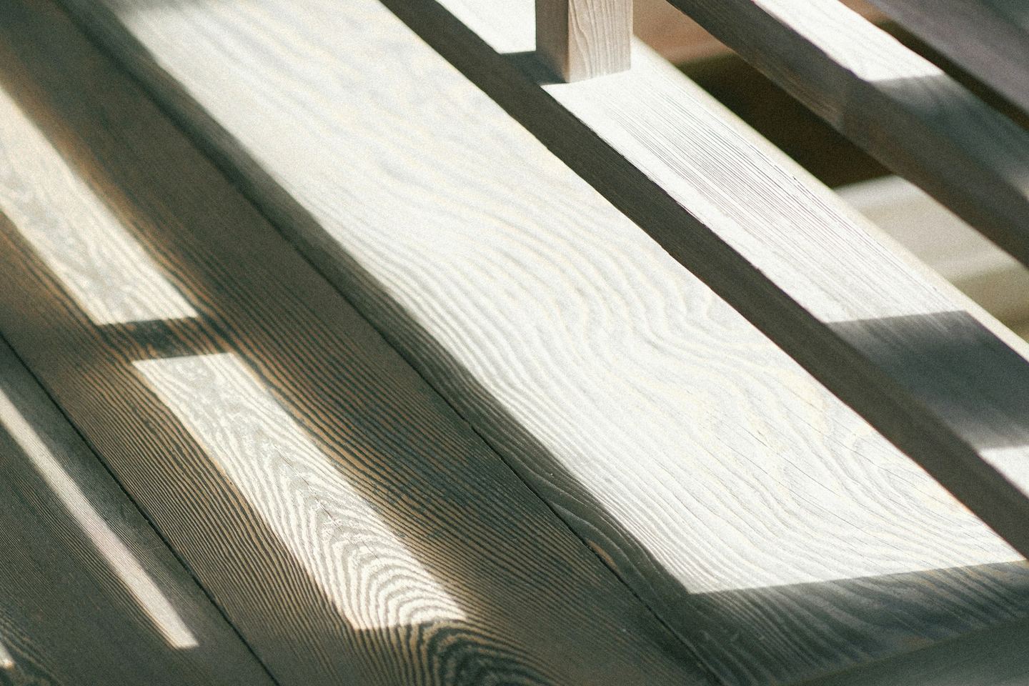 A plain wooden bench in sunlight, the light striped across its boards.