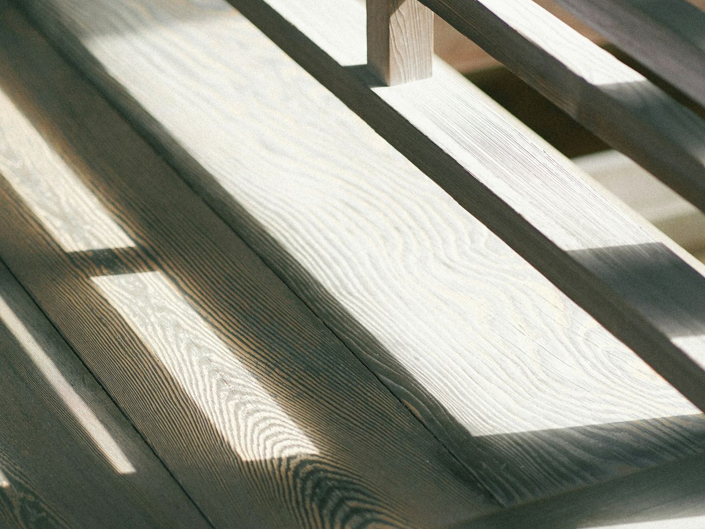 A plain wooden bench in sunlight, the light striped across its boards.