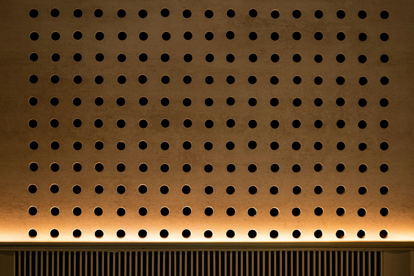 A wooden wall perforated with circular holes.