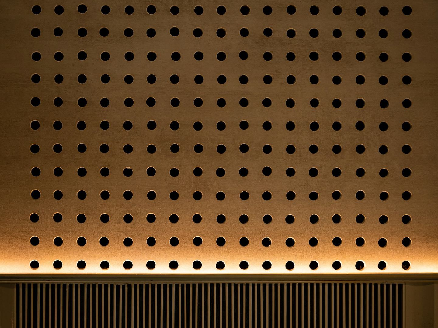 A wooden wall perforated with circular holes.